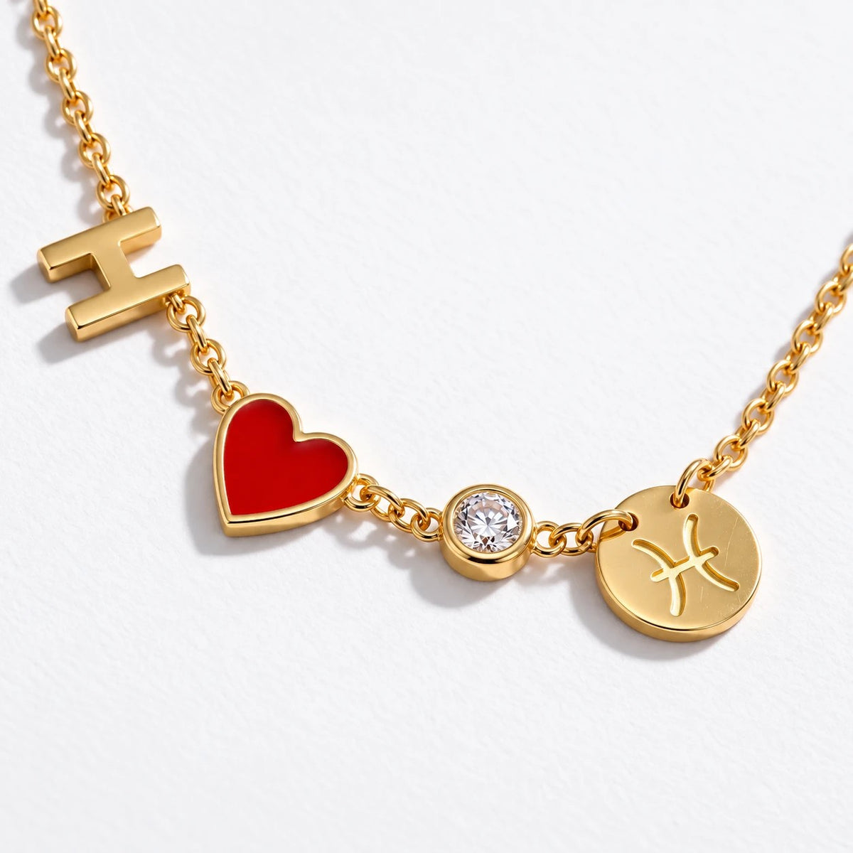 Close-up of gold pendants: letter H, red heart, crystal and Pisces sign