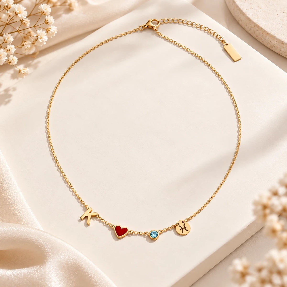 Gold necklace with K, red heart, blue birthstone and Pisces laid flat